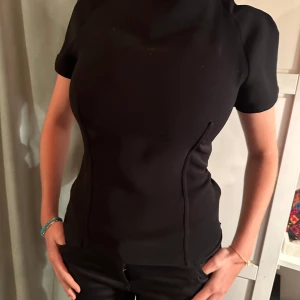 Fest topp - Nyskick, prislapp sitter kvar. Finare topp i kostym material. Två sömmar längst framsidan och baksidan. Har dragkedja i sidan och i bak.