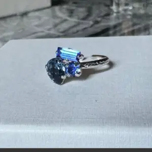Endast använd en gång! Vacker blå ring med en vacker kombination av tre olika kristaller med unika former.   Matchande armband finns bland mina andra annonser. Skickas i orginalask om man köper båda smyckena.   Modell: Isa Ringstorlek: justerbar