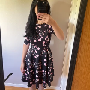 Blommig midiklänning - Svart klänning med rosa blommor från bodyflirt. Storlek XS och väldigt rejält material. Säljer då jag aldrig använder den 💕