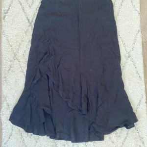 Svart Volang Kjol - Säljer denna då den är för liten för mig! A-linje kjol med slits och volanger. Den är inte strykt på bilden men ser bättre ut som den är det! Skönt material!