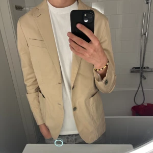 Oscar Jacobsson Kavaj - Tjena säljer min feta kavaj från Oscar Jacobsson, den är perfekt att ha nu inför sommaren med en snygg beige färg. Köptes förra sommaren men är fortfarande i perfekt skick.  Nypris, ca 5k men säljer för 2k, Priset kan diskuteras vid snabb affär✅