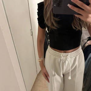 Svart topp med volangdetaljer - En svart topp med volangdetaljer på ärmarna. Toppen är kortärmad och har en rund halsringning.