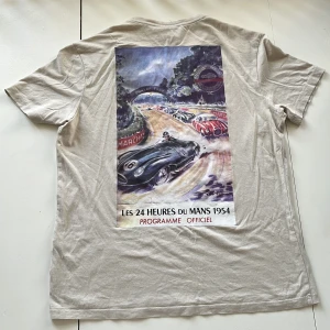 Beige t-shirt med bil tryck - Beige t-shirt från Bershka med text tryck på framsidan bild av ett bilrace på baksidan. T-shirten har korta ärmar och en rund halsringning och är i bra skick.