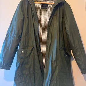 Regnjacka  - En oliv randig inuti regnjacka som är ny. Blir krispigt på grund av ja la i en påse bara.! 