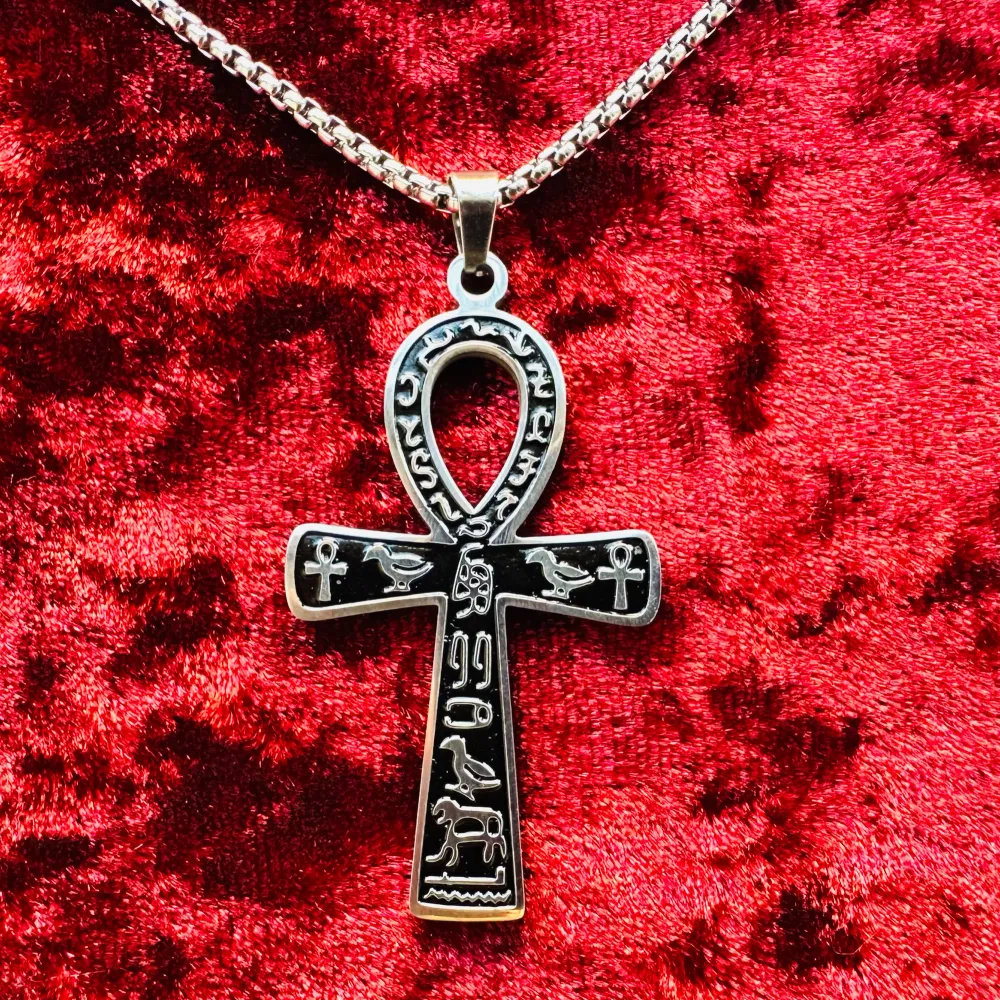 Nytt silverfärgat och svart halsband i rostfritt stål med ankh-symbol. Stilrent och kraftfullt. Amuletten är 5,cm lång x 3 cm bred. 60 cm ormkedja. Hummerlås. Den forntida egyptiska symbolen anses stå för evigt liv, odödlighet & reinkarnation.. Asusteet.