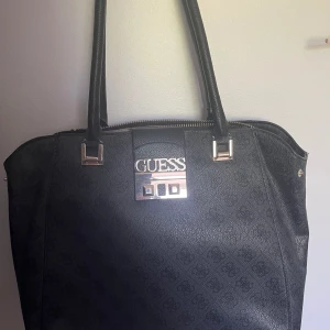Guess väska - Större väska från Guess, sparsamt använd med mindre tecken på användning, bra skick! Tillhörande dustbag kommer med! 4 små fack i väskan och ett på baksidan! 