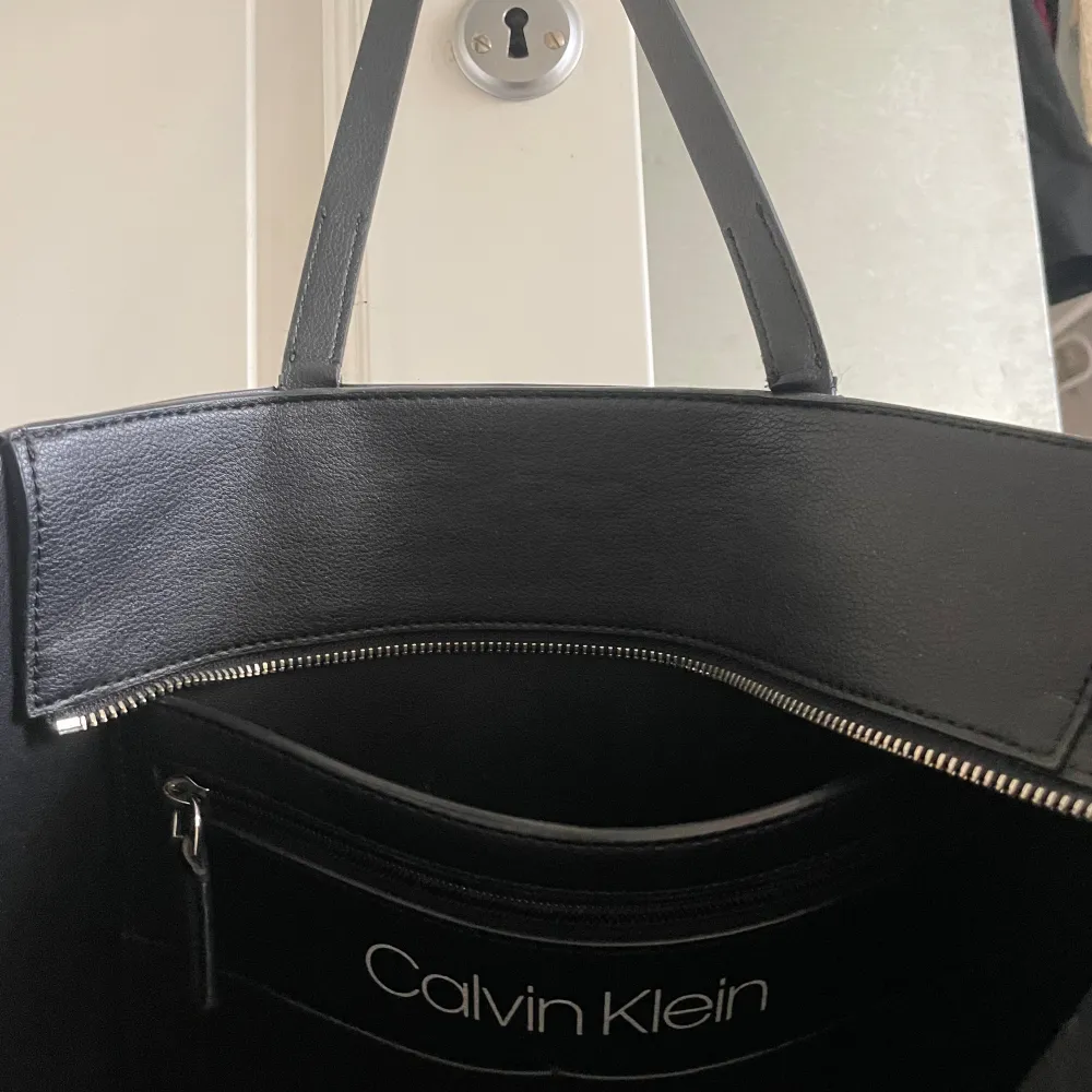 Jätte fin och stor handväska från Calvin Klein, perfekt som skolväska eller ens dagliga väska. Jätte bra skick, med två fack, varav ett av de går att stänga med dragkedja. Har små ”fläckar” av skinn som lossat, (bild 3). Modelen finns inte längre. . Övrigt.