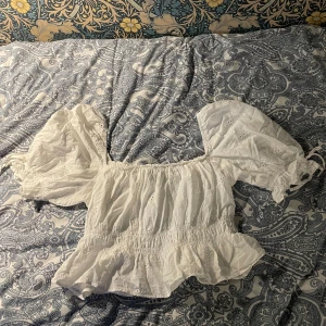 Vit blus - Det är en vit blus med puff ärm och är lite kortare, det är Blomdetaljer på den och även skrunch under byst och runt armen