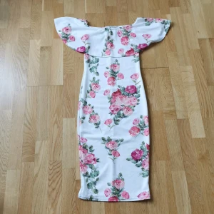 Vit klänning - Vit off shoulder klänning med blom motiv. Använd en gång. Från Nelly. Passar perfekt till en skolavslutning eller event. Den är i storlek XS men den passar defentivt S och kanske  pear shaped M då den är strechig. 