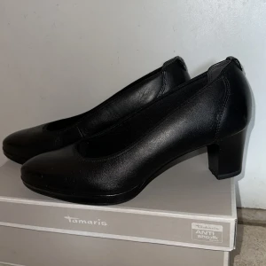 Tamaris klacksko - Nyskick på Tamaris klacksko. Endast använda en gång. Köpta i mitten av mars. Svart skinn. 