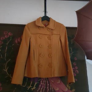 Kort kappa impuls - 💛Senapsgul kort kappa💛  Storlek 32. XS.   Yttertyg: 60% ull, 40% viskos Foder: 100% polyester   HM impuls början av 2000 talet. Inte använd på över 15 år.   Fint skick. Nån lös tråd. Några noppor, flesta dras lätt bort.   Mer bilder finns