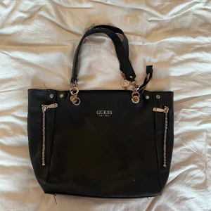 Guess handväska svart - Guess handväska. OK skick, men välanvänd. Slitage på handtagen + insidan av väskan, därav det låga priset!  Köparen står för frakten!    Fråga mig om fler bilder och fraktpris. 