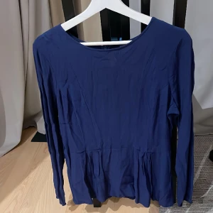 Blå blus - En jättefin blå blus med en liten volangkant.  Dragkedja i bak  Storlek 42