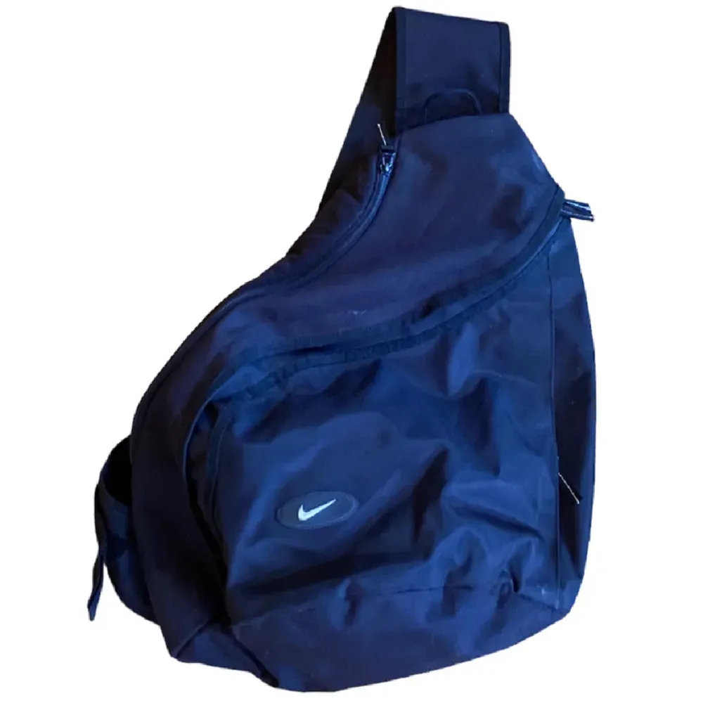 En vintage Nike slingbag. Slingbagen är i extremt bra skick och väldigt sällsynt. Man får plats med mycket i de två större utrymmena, finns även mindre fack för nycklar osv. Vid fler frågor tveka inte att kontakta oss!. Väskor.