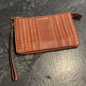 Michael Kors - Liten väska Michael Kors, äkta och inköpt i New York. Aldrig använd så helt i nyskick. Flera fack för kort och annat smått. Vinröd med gulddetaljer Mått: 20 cm 13,5 cm  