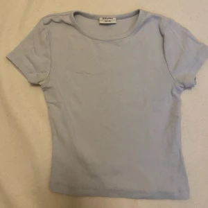 Ljusblå t-shirt  - En ljusblå t-shirt med små ränder i tyget. Från KappAhl och storlek 146-152. Ganska kort i magen, men inte riktigt lika kort som en magtröja.