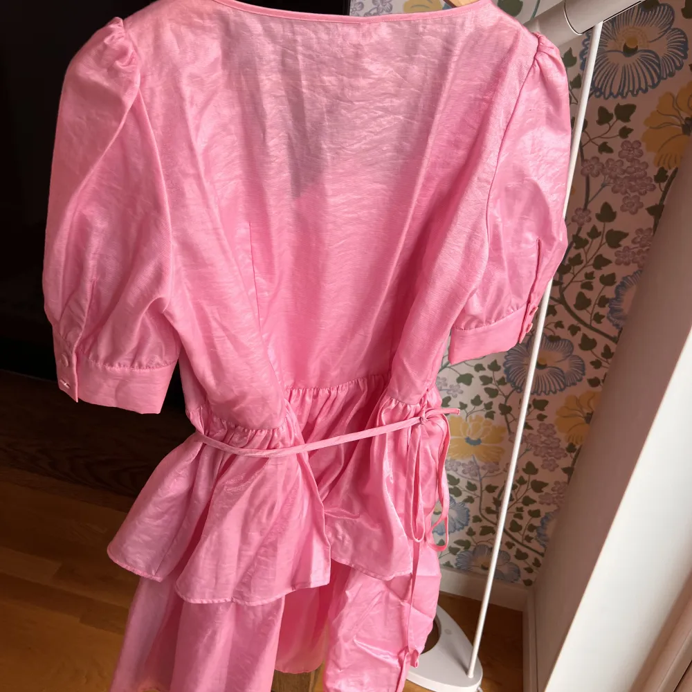 Helt oanvänd, fin rosa kortare klänning med knyte omlott i midjan. Fint skimrande tyg, med underklänning i. Nypris :1900kr.. Klänningar.
