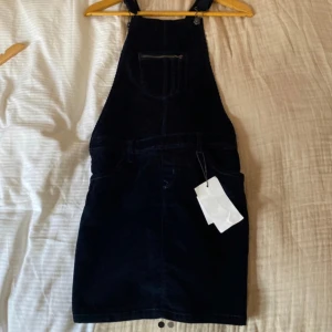 Byxdress - Mörkblå hängseldress i manchestertyg fast som är som en kjol nertill även kallad ”bibskirt” i barnstorlek.