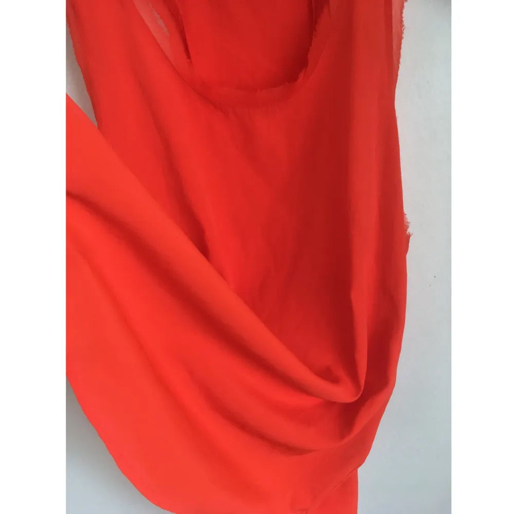 Orange linne i vävt material med råa kanter i chiffong, rundad nederdel. Mått i cm: bröstvidd 46; axelbredd 27; längd fram från axeln 68. . Toppar.