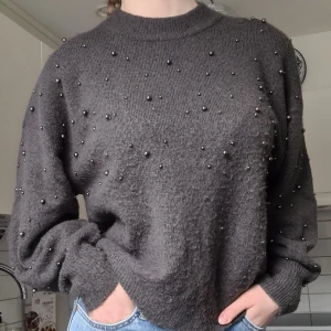 Stickad tröja pärlor  - Mörkgrå stickad tröja med pärlor. Använd men i fint skick, har en avslappnad passform.  Material: 52% Polyester, 41% Akryl, 4% Ull, 3% Elastan. 