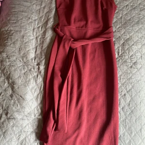 One shoulder klänning med knytband i midjan  - Burgundy one shoulder midiklänning med bälte i midjan. Klänningen är stretchiga. Endast använd en gång 