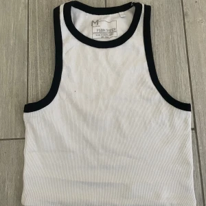 Kort vitt linne med svarta detaljer - Använt få gånger i bra skick. Jättefint inför sommaren till en brunbränd mage! Den slutar precis vid midjan. 