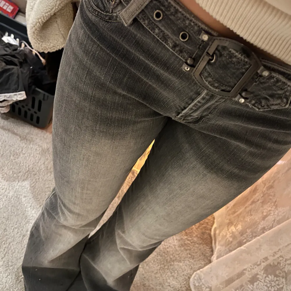 Lågmidjade vintage jeans med utsvängda ben och bälte. Glittriga detaljer längstner på jeansen och bakfickor i en lite mörkare kontrast färg.   Mått:  Midja: 40 cm  Ytterbenslängd: 102 cm  Innerbenslängd: 78 cm  Gren: 23 cm . Jeans & Byxor.