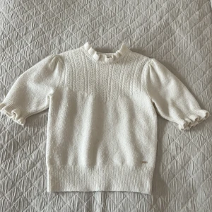 Stickad T-shirt  - En stickad krämfärgad T-shirt med puffärm från Holly and Whyte (Lindex). Fint stickat mönster på bröstkorgen.