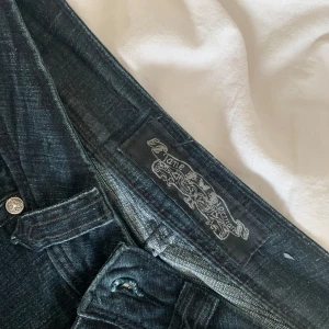 Lågmidjade bootcut jeans - Mörka jeans med fina detaljer på bakfickorna. Passar mig med storlek xs som är 165 lång. Fint skick förutom några av stenarna på fickorna som har ramlat av.