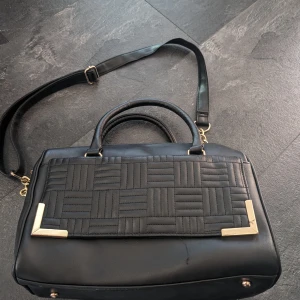 Svart väska  - Svart väska med gulddetaljer. 32*23*14 cm