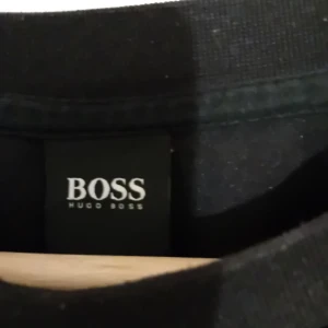 Tröja Boss - Svart långärmad tröja med guld tryck från Boss. Strl M