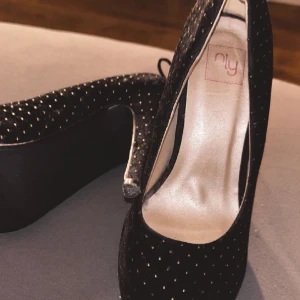 Klackskor - Svarta klackskor med ”mocka”? ”samet”? Mateial med rosett där bak från nelly.