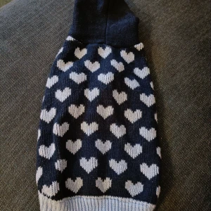 Söt stickad hundtröja med luva  - Ryggmått ca 30cm. Sparsamt använd. Har använts av hårlös hund, så inga pälsrester finns. Det har funnits en stor tofs på luvan som jag har klippt bort se bild.