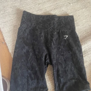 Svarta träningsshorts från Gymshark - Svarta träningsshorts från Gymshark med ett diskret mönster. Shortsen har en hög midja och är knälånga med detalj som gör att de sitter bra i rumpan
