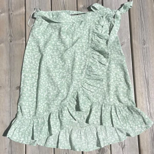 Amelie&me- grön blommig kjol - Super fin och söt kjol som man kan knyta. Endast använd några gånger och är i nyskick. Jättebra att ha på sommaren men säljs då den inte passar längre.