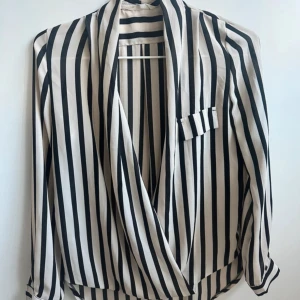 Randig blus - Fin randig blus. Finns ingen knapp att stänga med, så det är meningen att den ska vara öppen (man kan tex ha ett fint linne under). Lite längre baktill.