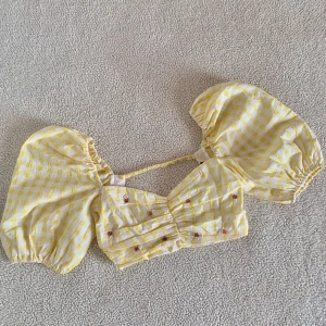 ZARA gul gingham crop top med ballongärmar - Otroligt vacker gingham topp från ZARA med pärlor och ballongärmar. Använd en gång. Storlek XS men passar definitivt även en S. Saknade en röd blomma när jag köpte den, i övrigt i nyskick. Öppen rygg. Skickar fler bilder vid intresse 🌹