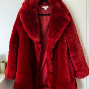 röd päls jacka - En längre vintage faux päls jacka, jag är 167 och den går ner till mitten av låren på mig ungefär. bra skick, köpt på vinted men sälja vidare pga att jag inte användt❣️