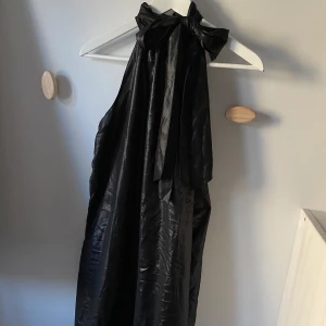 Halterneck klänning - Svart klänning med halterneck och snöre som kan knytas på olika sätt. Saknas 3 knappar i nacken men annars fint skick.