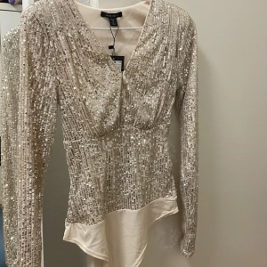 Glittrig body - Super fin body som sitter tajt vid midjan. Jag har sytt in den vid brösten men det är väldigt lätt att sprätta upp den. (Helt oanvänd prislapp finns)