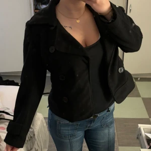 Svart kort kappa - En svart kort kappa med knappar. Sönder inne i kappan( se sista bilden). Säljer därför för långt pris