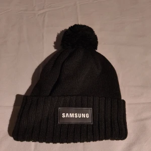 Svart mössa från Samsung | oanvänd - Helt ny svart mössa från Samsung med en tofs på toppen. 