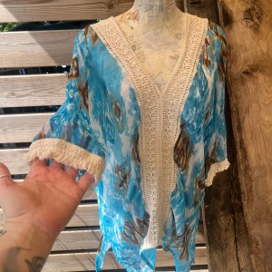 Härlig blus/strandklänning med virkade detaljer  - Härlig tunika/blus/strandklänning i vitt, turkosblå, brunt batik mönster som är väldigt skirt/luftigt samt vackra detaljer i byst och ärmslut som är virkade. Fint skick! Stl M 