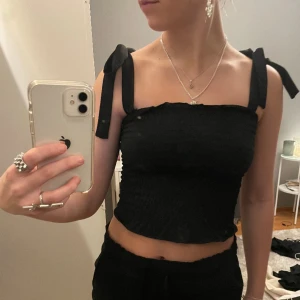 Topp - Säljer denna fina svarta ribbade topp med rosetter på axlarna💕