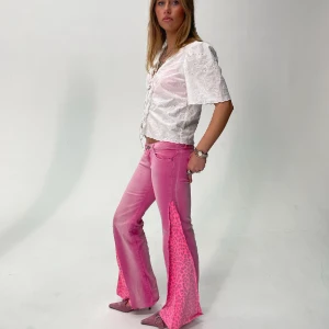 REMAKE PINK CHEETAH JEANS - Storlek: Midja (70cm), Innerbenslängd (79cm), total längd (95). Rosa, remake, lågmidjade, bootcut jeans med rosa leopardmönstrad slit. Modellen är 172cm.