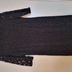 Svart, knälång spetsklänning med svart undertyg (ej ärmarna).