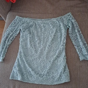 Ljusgrön spetsblus - En elegant ljusgrön spetsblus med blommönster. Blusen har långa ärmar och en off-shoulder design. Den är fodrad med ett mjukt tyg på insidan för extra komfort. ha använt den bara 1 gång. är 100% ny.