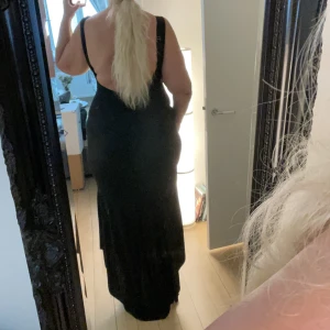Svart lång klänning xl - Lång svart klänning. Lite mermaid stil då den är längre bak, som ett litet släp. Djup öppning i rygg mot rumpan, stängd fram. Polyestermaterial, lätt stretch