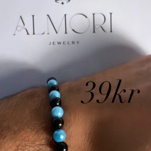 Armband från Almori - Ett stilrent armband från Almori med pärlor i blått och svart. Armbandet är elastiskt och passar de flesta handleder.