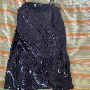 Svart paljettklänning - En lila klänning täckt med glittriga paljetter. Klänningen har smala axelband och en v-ringad halslinje. Perfekt för festliga tillfällen.